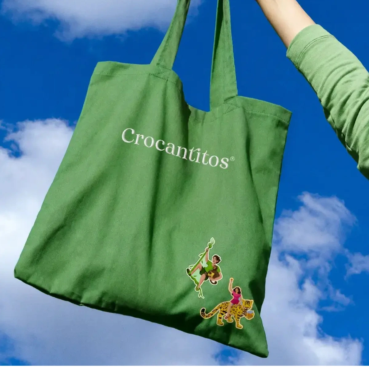 Caso de estudio Crocantitos: Bolsa de tela verde con el logotipo Crocantitos sostenida en alto contra el cielo.